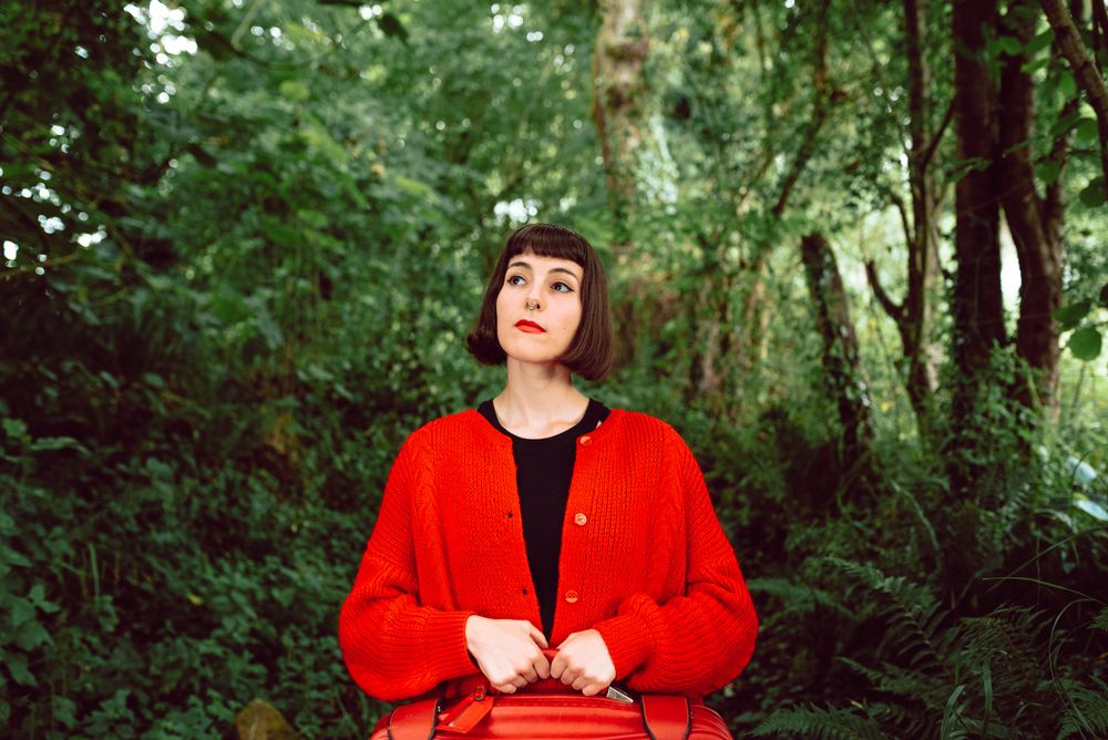 Woman in red with big red suitcase in forest