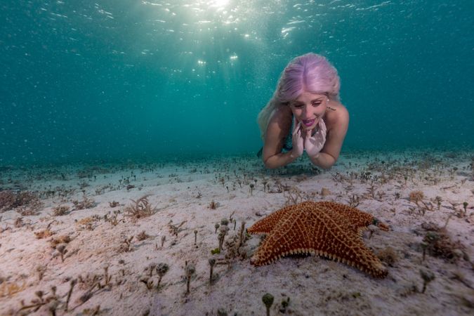 Redhead fairytale female mermaid swimming beside starfish