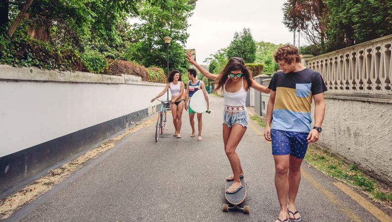 Happy young woman riding on skateboard with her friends