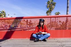 Woman in red sitting cross legged using a mobile phone outdoors