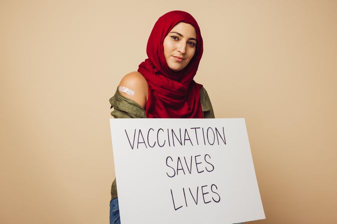 Muslim woman holding a signboard with "vaccination saves lives"
