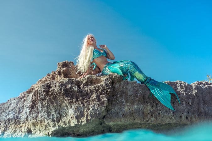 Blond fairytale female mermaid lying on rock