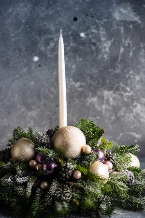 Side view of purple and gold Christmas centerpiece with candle in pine branch on table