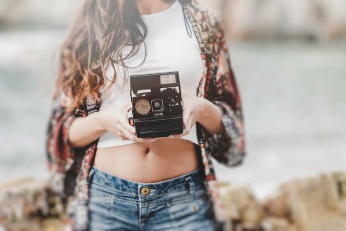 Woman with camera on shore near stones and water
