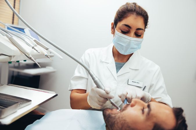 Woman dental doctor using tools to check teeth of male patient