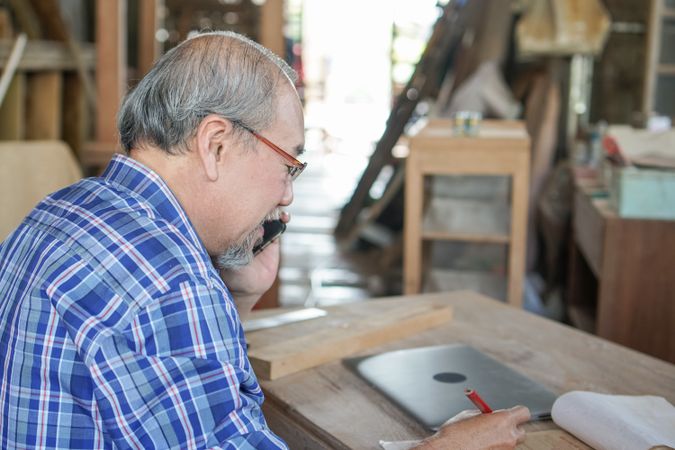 Asian carpenter on phone in workshop