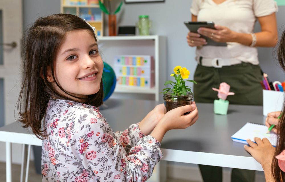 Female student looking at camera while holding a pansy plant in ecology classroom