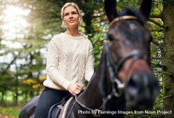 Beautiful woman sitting astride on her mare horse outdoors bxakr0
