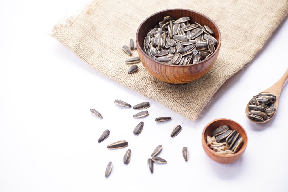 Sunflower seeds in wooden bowl and wooden spoon on table with brown cloth