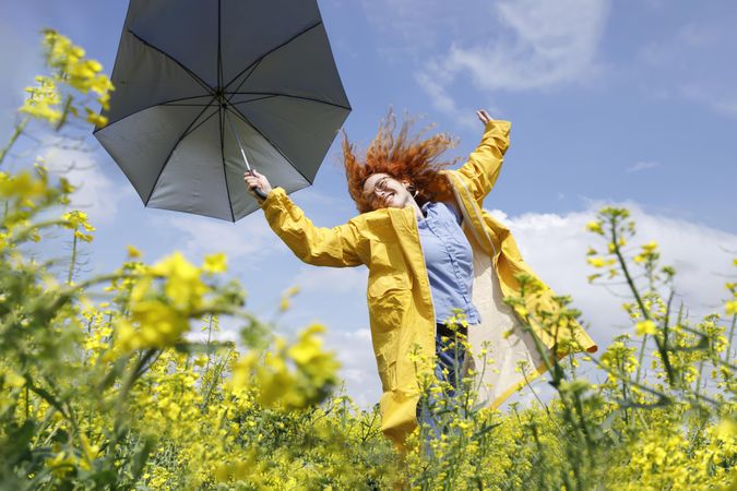 Red haired woman dancing in a yellow field holding umbrella