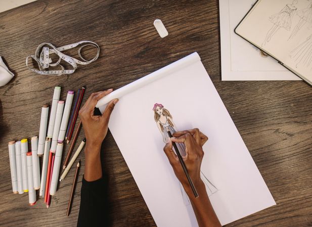 Top view of fashion designer sketching a design sitting at wooden table