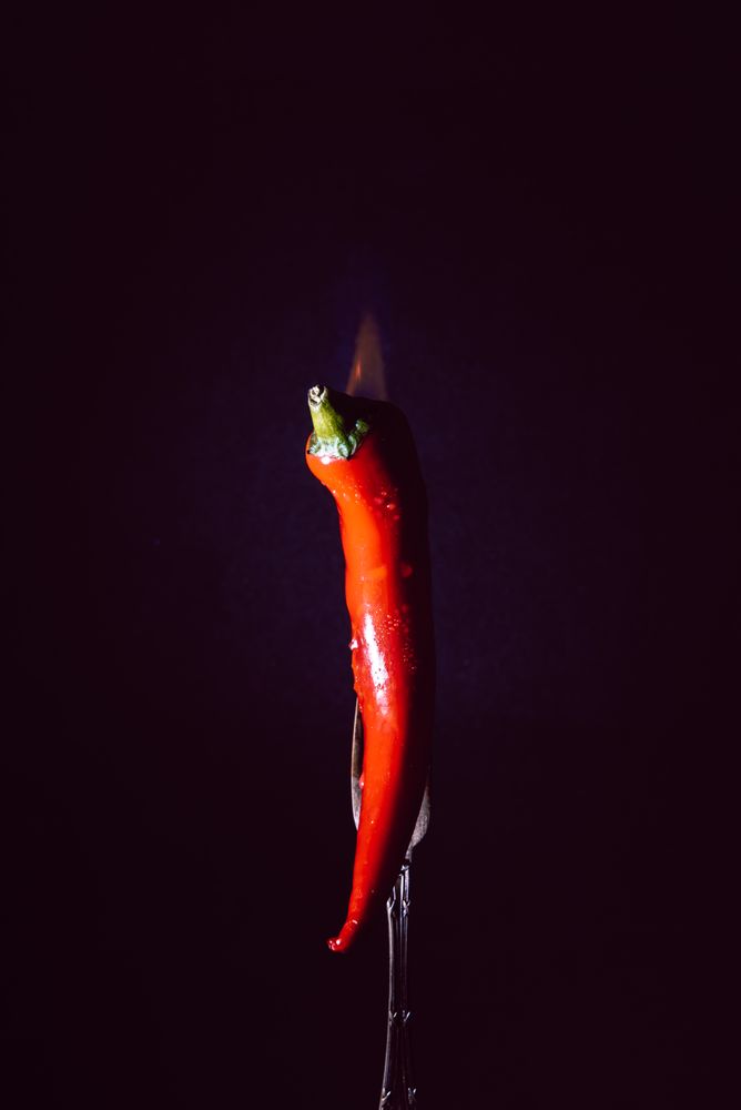 red chili pepper on fire in fork on a dark background