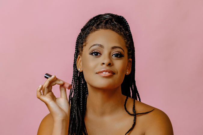 Confident Black woman holding lip gloss while looking at camera