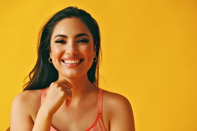 Headshot of laughing Hispanic woman with one hand reaching to her face in yellow room