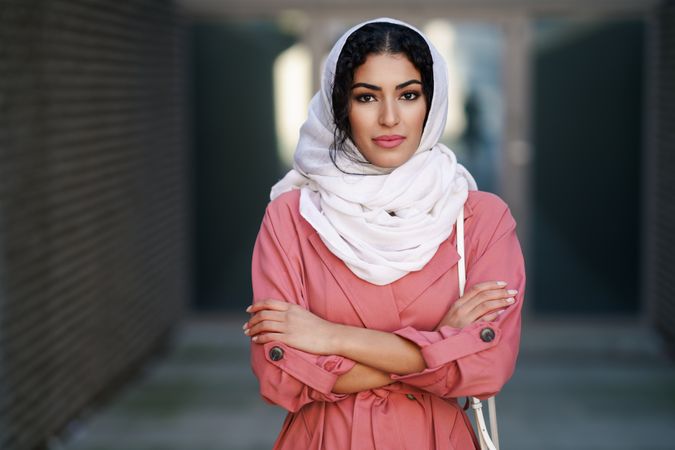 Female in headscarf and pink trench coat standing confidently with her arms crossed