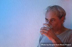 Portrait of middle aged man in gray shirt drinking water against light background in UV lit studio 0J2pd0