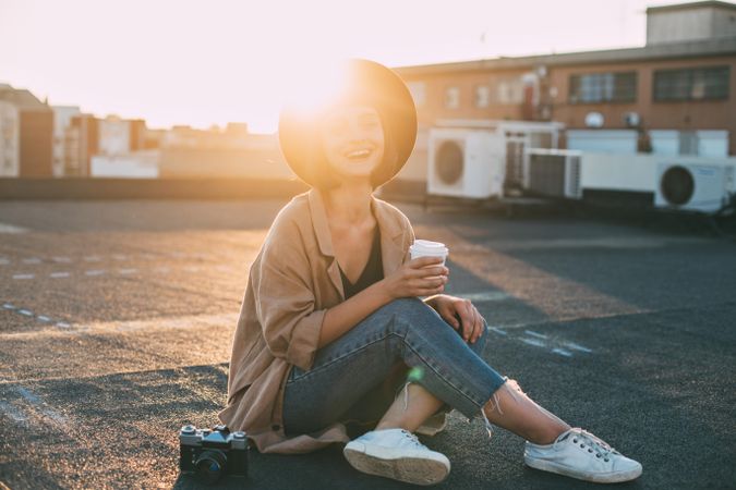 Backlit woman smiling on rooftop with coffee