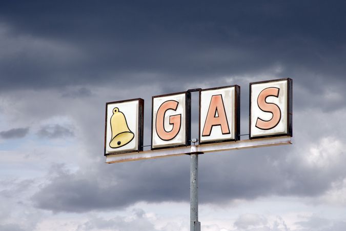 Weathered gas station sign against dark storm clouds