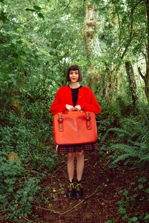Woman in red with big red suitcase in forest