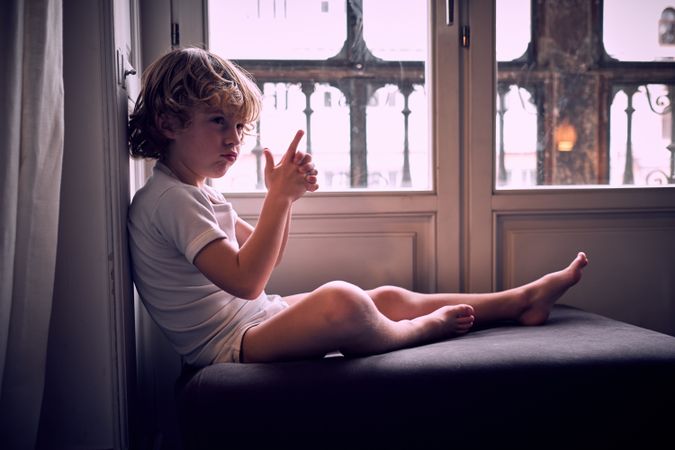 Adorable kid doing gun gesture with fingers at home