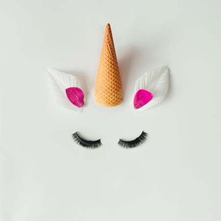 Unicorn head with petals and ice cream cone on light background