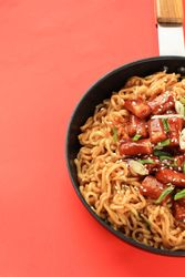 Pan of noodles topped with Korean rice cakes in red studio