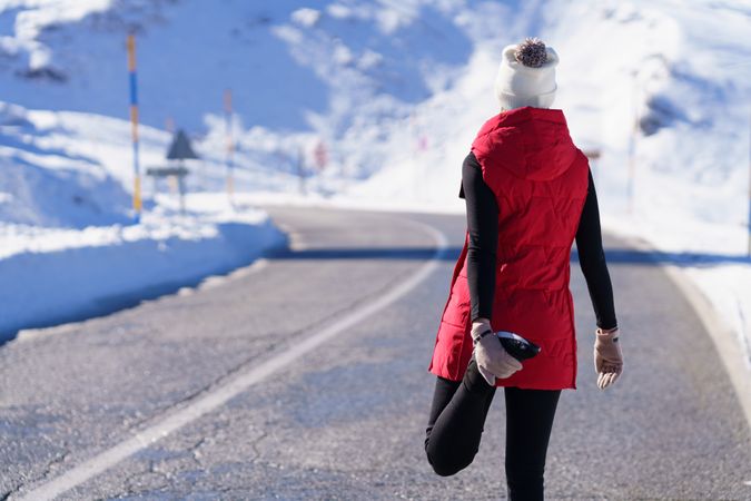 Back of fit woman in wintry gear stretching quadriceps in the mountains on cold day