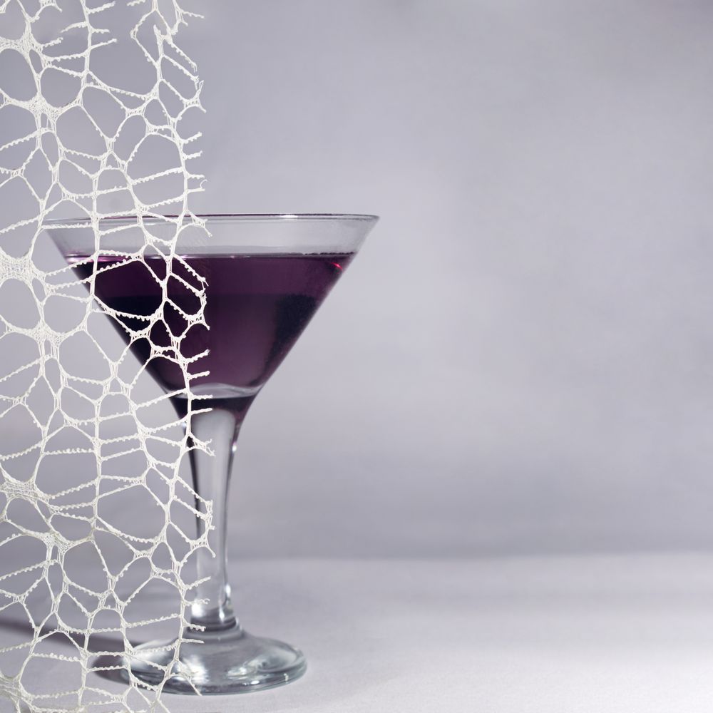 Dark cocktail in martini glass behind lace