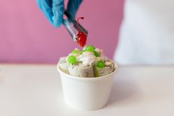A worker is decorating a rolled ice cream tub with a cherry on top using tongs