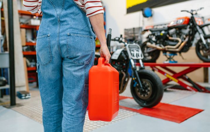 Back view of mechanic woman holding jerry can in front of motorcycles on factory