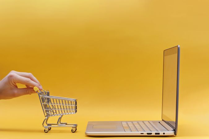 Online Shopping Concept with Mini Cart and Laptop on Yellow Background