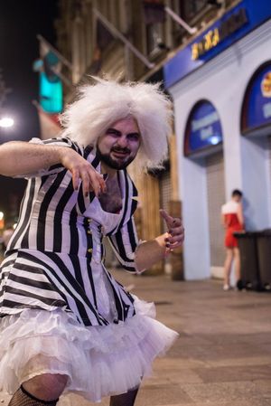 Young man partying in street wearing Beetlejuice tutu drag costume in Halloween monster pose