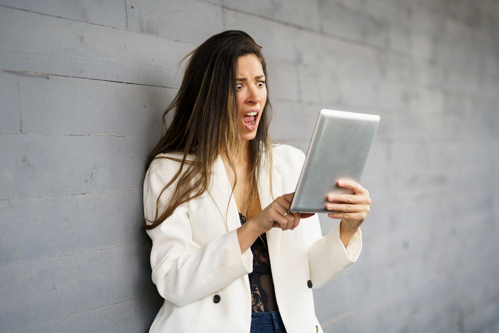 A shocked woman is reacting to breaking news she is reading on her tablet against a gray wall