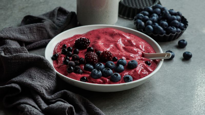 Smoothy of fresh bog blueberries and raspberries in bowl near napkin