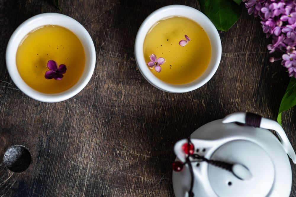 Top view of teapot with cups with delicate tea and pink flowers