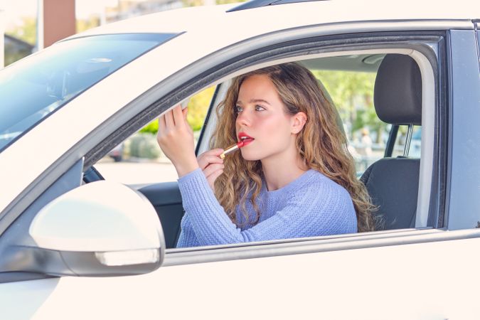 Young woman applying red lipstick in modern car on parking