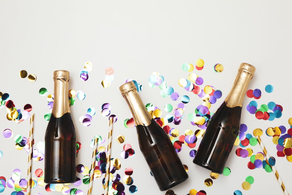Composition with mini champagne bottles and glitter on light background, copy space