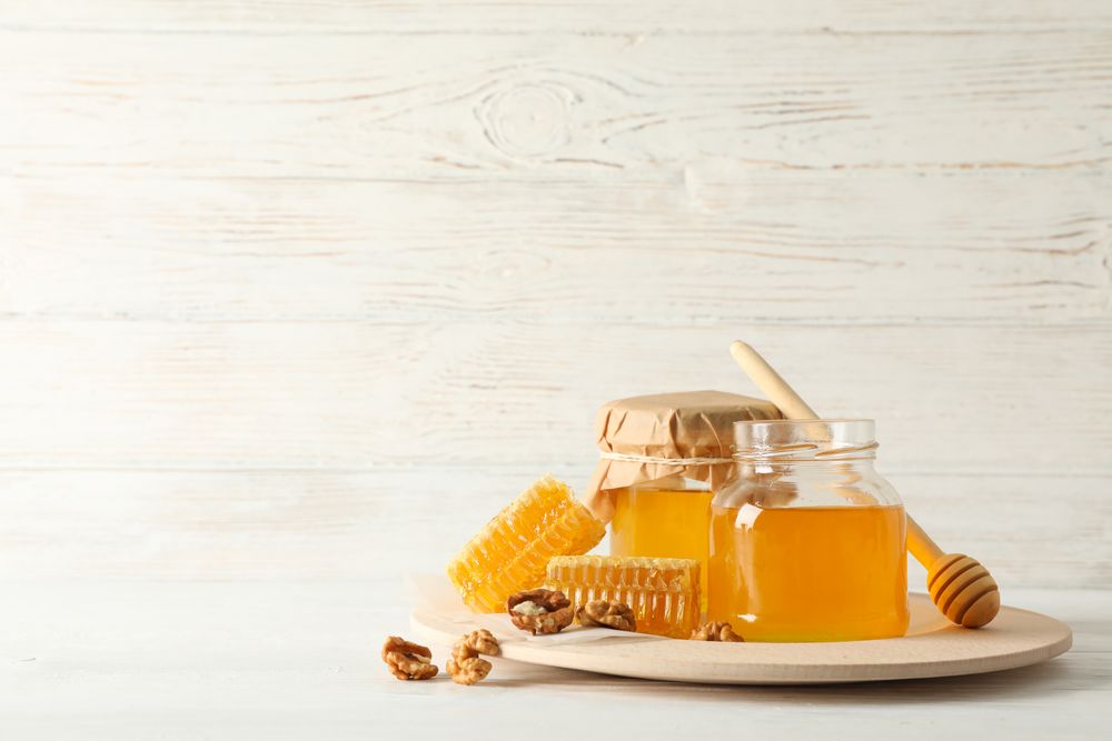 Honeycombs, walnuts, dipper and jars with honey on wooden background, copy space