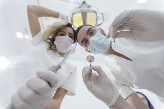 Dentists wearing surgical mask while holding angled mirror and drill, ready to begin exam