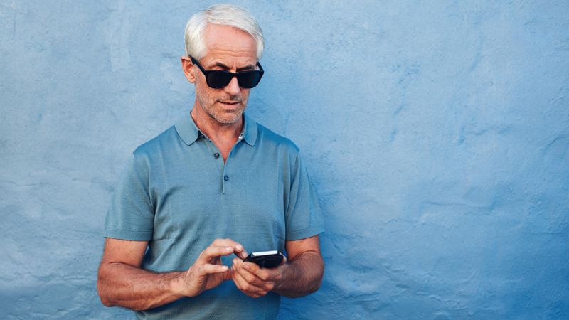 Portrait of mature man in sunglasses reading text message