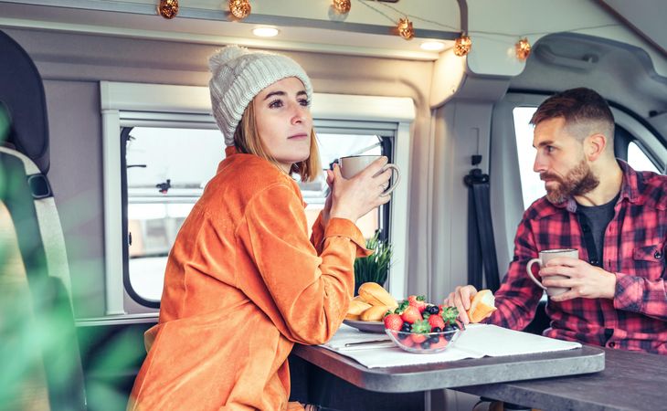 Male and female friend enjoying breakfast and sipping coffee while enjoying the view in back of van