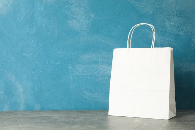 paper bag on grey table against blue background, copy space