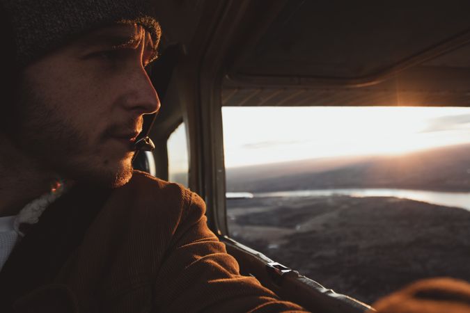 Man inside helicopter looking down river and mountains during sunset