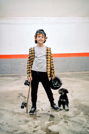 Satisfied kid with helmet and skateboard against dog on street