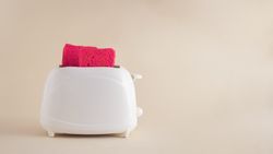 Pink toast coming out of toaster on a soft bright beige background