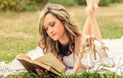 Romantic woman with shoes in the hand reading a book outdoors