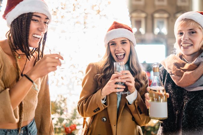 Three happy young women laughing and celebrating with champagne at Christmas.