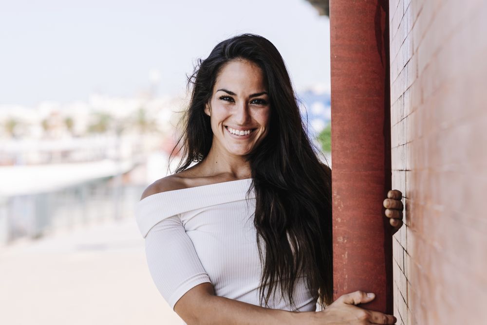 smiling young woman hanging on a pole in the street while looking camera
