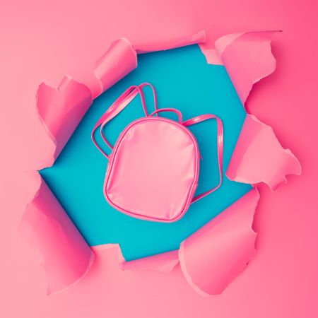 Torn pink paper revealing backpack underneath on blue background