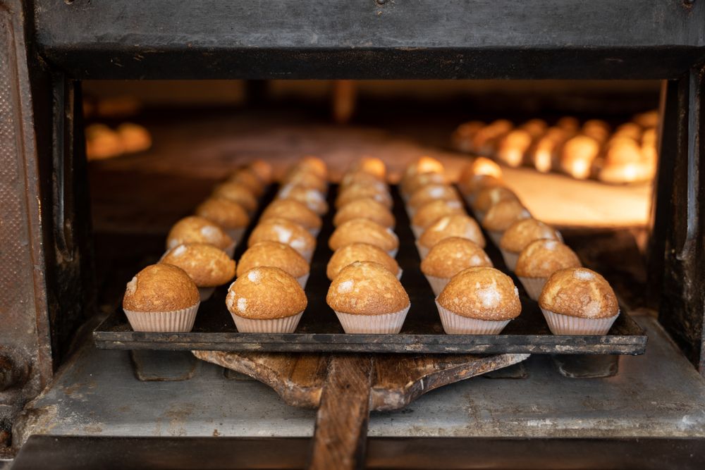 Some cupcakes tray freshly baked are being pulled from a stone oven with wooden shovel